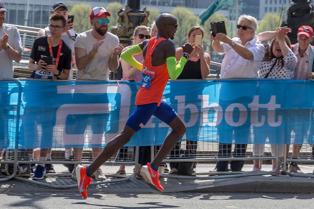 Maratonløber i farvestrålende løbetøj, inklusive armærmer til solbeskyttelse, løber på en solrig rute med tilskuere.
